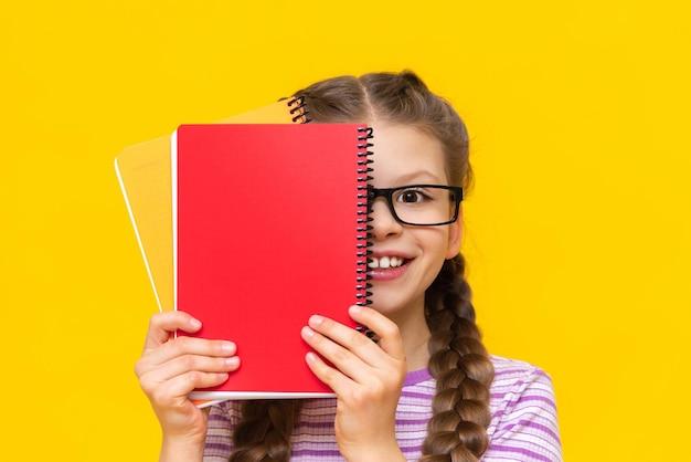 Una bella bambina si affaccia da dietro un quaderno rosso e sorride Una studentessa su uno sfondo giallo isolato