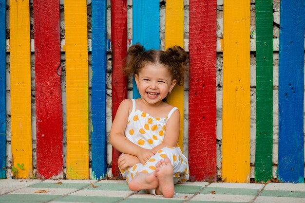 Una bella bambina si siede vicino a un recinto di legno multicolore