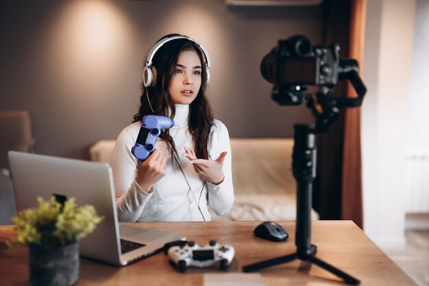 Una bella blogger sorpresa in cuffia è in streaming in diretta parlando di videogiochi. Influencer giovane donna live streaming tenere il joystick.