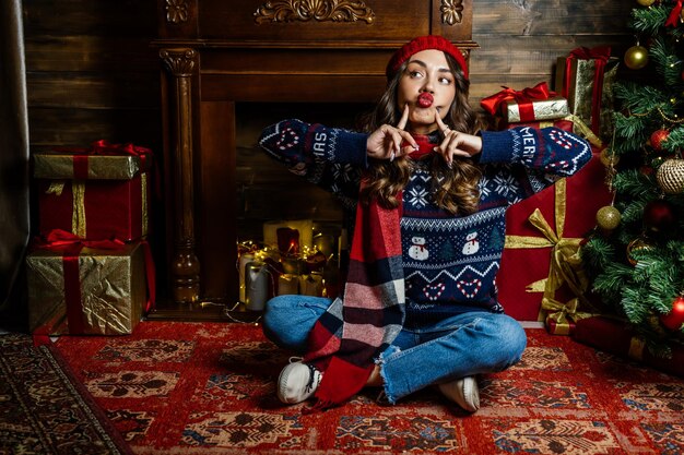 Una bella bruna siede sotto un albero di Natale sullo sfondo delle decorazioni di Capodanno