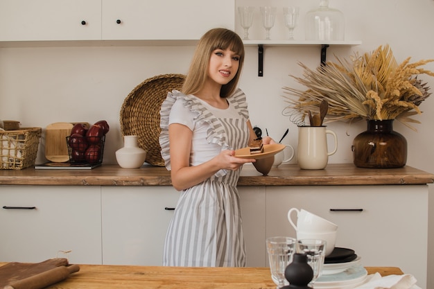 Una bella casalinga con un grembiule grigio sta in cucina e tiene un piatto con il dessert