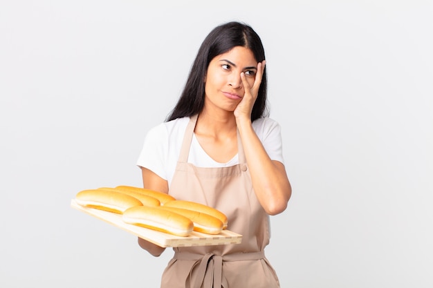 Una bella chef ispanica che si sente annoiata, frustrata e assonnata dopo una noiosa e con in mano un vassoio con focacce di pane