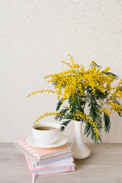 Una bella composizione di rami di mimosa e una tazza da tè bianca con un piattino e una pila