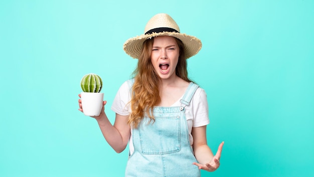 Una bella contadina dai capelli rossi che sembra arrabbiata, infastidita e frustrata e tiene in mano un cactus