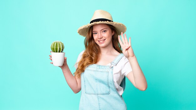 Una bella contadina dai capelli rossi che sorride e sembra amichevole, mostra il numero quattro e tiene in mano un cactus