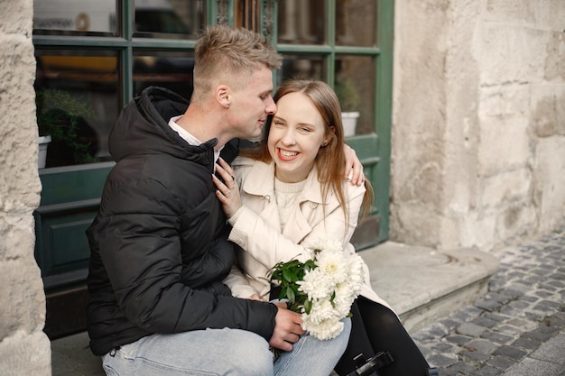 Una bella coppia che si abbraccia e si bacia per strada in autunno Uomo e donna con in mano un mazzo di fiori in una strada della città vecchia Ragazza che indossa un cappotto beige e una giacca nera da uomo