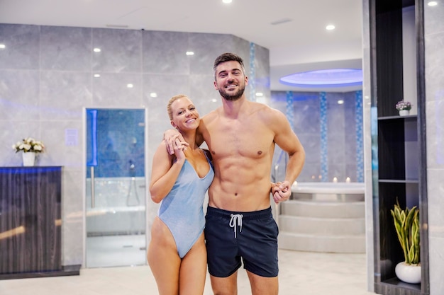 Una bella coppia felice in costume da bagno in piedi e avvolgente presso il centro termale Coppia alle terme
