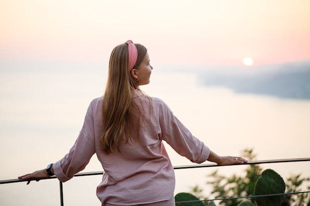 Una bella donna al tramonto si erge su una terrazza affacciata sul mare. Foto di alta qualità