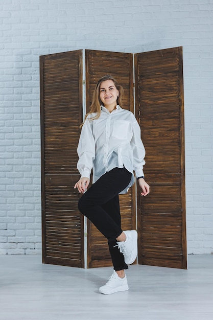 Una bella donna alla moda indossa una camicia di cotone bianca e pantaloni neri Ragazza emotiva allegra in scarpe da ginnastica bianche