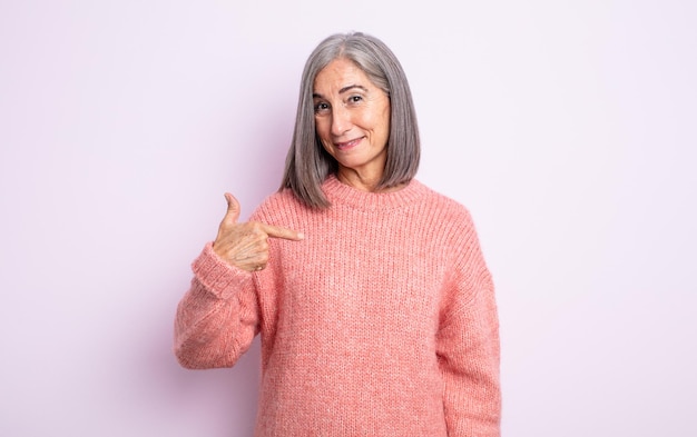 Una bella donna anziana che sembra orgogliosa, fiduciosa e felice, sorridente e che indica se stessa o fa il segno numero uno