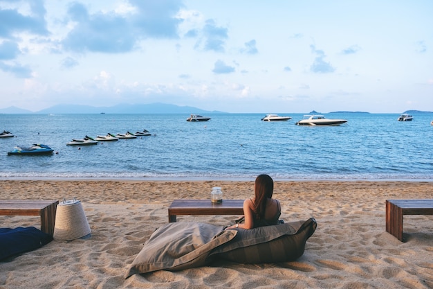 Una bella donna asiatica ama sedersi e rilassarsi sulla spiaggia in riva al mare