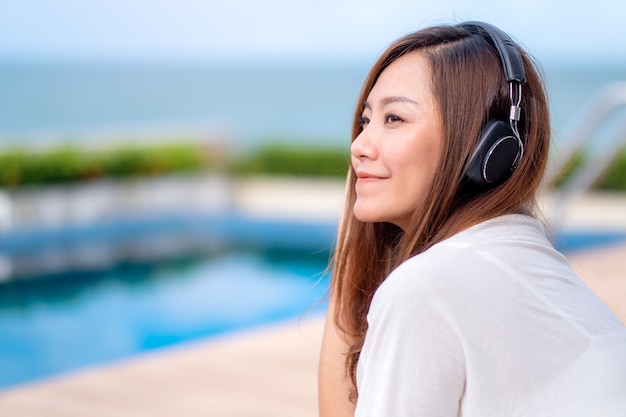 Una bella donna asiatica che ascolta musica con le cuffie mentre è seduta a bordo piscina