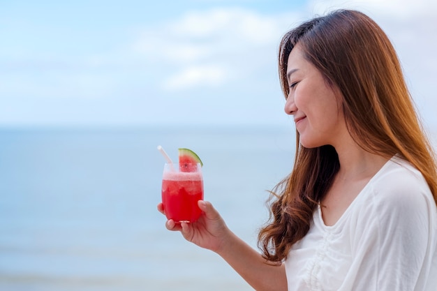 Una bella donna asiatica che beve succo di anguria mentre è seduta in riva al mare