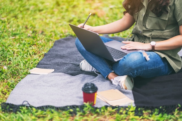 Una bella donna asiatica che lavora e digita sulla tastiera del laptop mentre è seduta nel parco