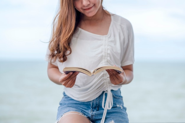 Una bella donna asiatica che legge un libro in riva al mare