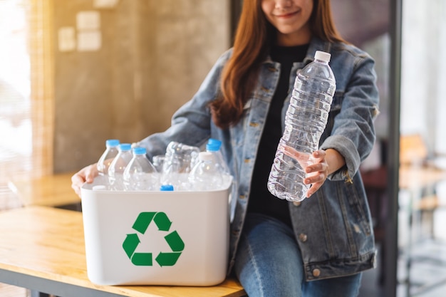 Una bella donna asiatica che tiene e che raccoglie le bottiglie di plastica riciclabili dell'immondizia in un bidone della spazzatura a casa