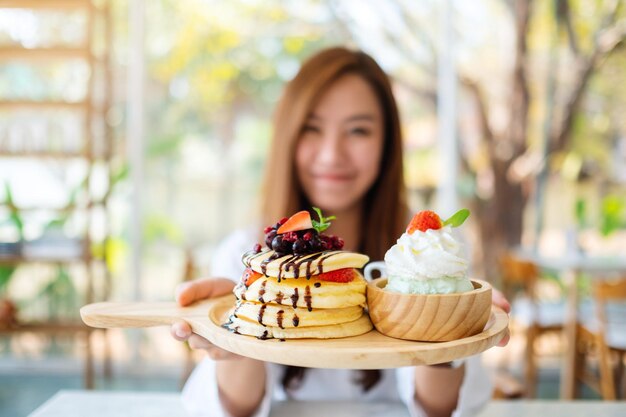 Una bella donna asiatica che tiene e mostra un piatto di frittelle con gelato e panna montata al caffè