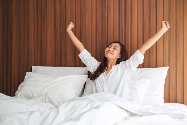 Una bella donna asiatica fa stretching dopo essersi svegliata la mattina su un letto accogliente bianco a casa