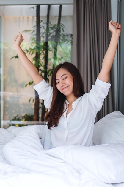 Una bella donna asiatica fa stretching dopo essersi svegliata la mattina su un letto bianco e accogliente a casa