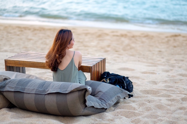 Una bella donna asiatica gode di seduta sulla spiaggia in riva al mare