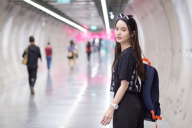 Una bella donna asiatica indossa una camicia nera, entra nel tunnel della metropolitana e tiene in mano lo zaino