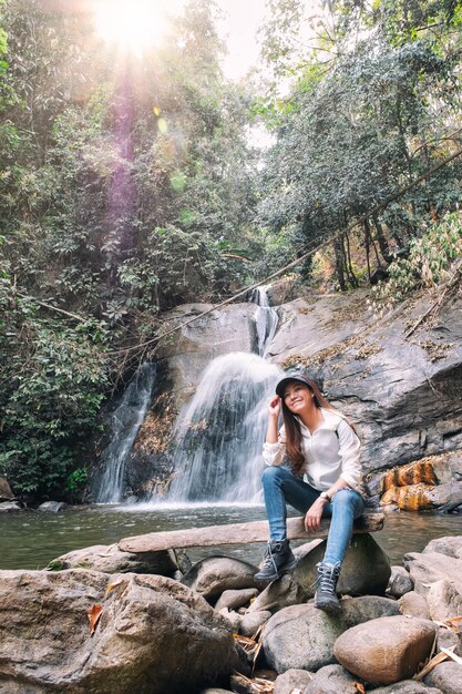 Una bella donna asiatica seduta davanti alla cascata nella giungla