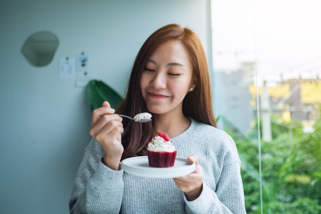 Una bella donna asiatica si è divertita a mangiare la torta della tazza di velluto rosso