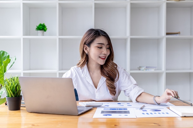 Una bella donna asiatica siede nel suo ufficio, una donna d'affari asiatica controlla i documenti finanziari di una società che lei e il suo partner hanno creato. Concetto di gestione finanziaria aziendale.