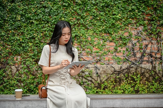 Una bella donna asiatica usa il suo tablet digitale mentre si rilassa su una panchina in città