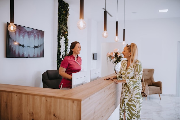 Una bella donna bionda che conversa con la receptionist della clinica odontoiatrica che fissa un appuntamento