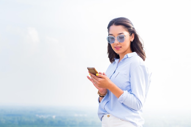 Una bella donna bruna con gli occhiali con gioia e un sorriso usa uno smartphone sorpreso