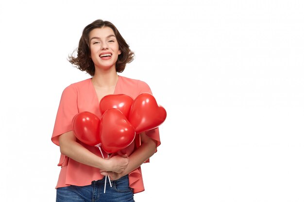 Una bella donna bruna con un largo sorriso in jeans e una giacca rosa con palloncini rossi a forma di cuore