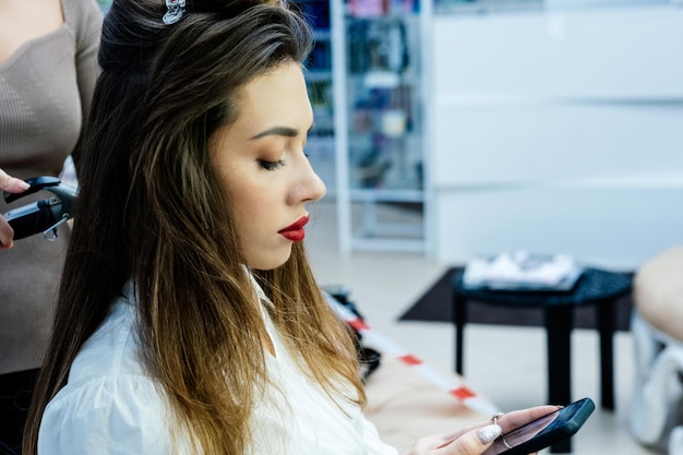 Una bella donna bruna usa il telefono mentre i suoi capelli vengono pettinati in un salone di bellezza.