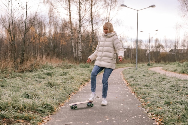 Una bella donna che fa skateboard in un parco autunnale, impara a pattinare sullo skateboard trascorrendo il fine settimana all'aria aperta all'aperto. Concetto di sport sano.