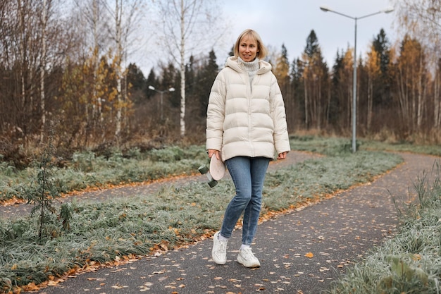 Una bella donna che fa skateboard in un parco autunnale impara a pattinare sullo skateboard trascorrendo il fine settimana