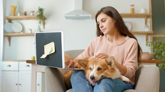 Una bella donna che lavora con un computer portatile e accarezza un cane carino. Donna che si sente spensierata e felice.