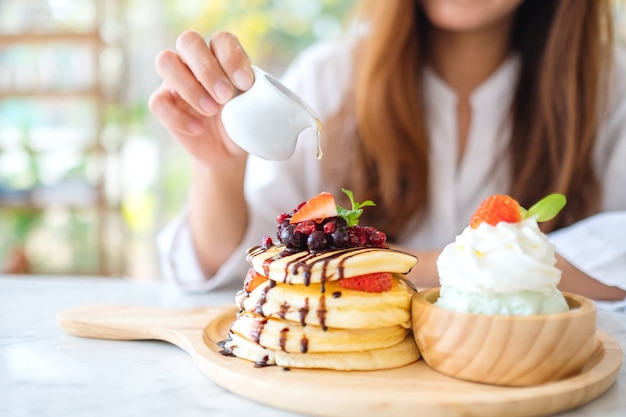 Una bella donna che versa il miele in un pezzo di pancake ai frutti di bosco con gelato e panna montata