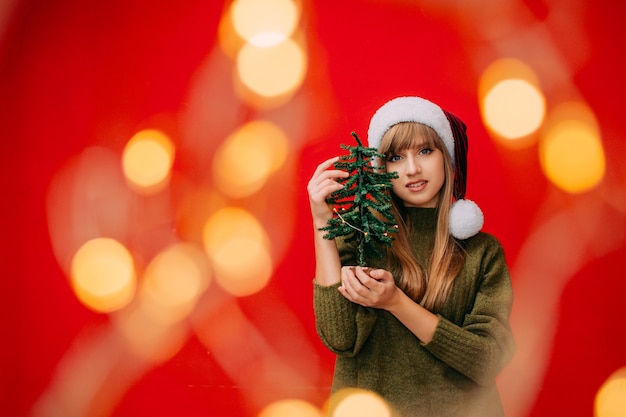 Una bella donna con un cappello da Babbo Natale tiene in mano un piccolo albero di Natale Concetto di capodanno