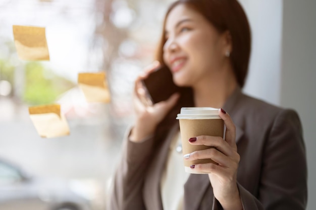 Una bella donna d'affari asiatica tiene la sua tazza di caffè mentre parla al telefono