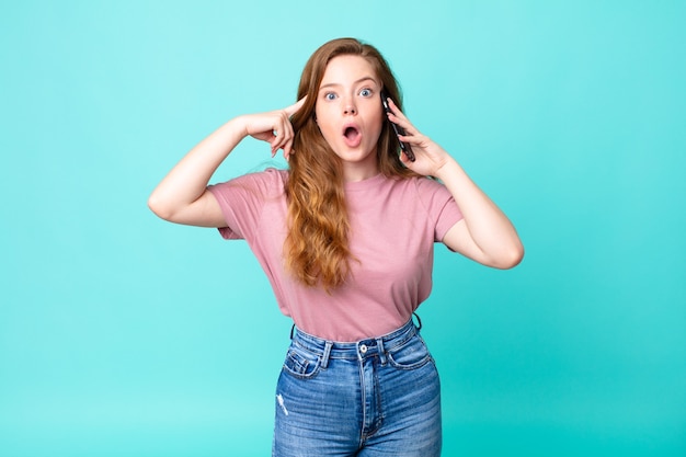 Una bella donna dai capelli rossi che sembra sorpresa, realizzando un nuovo pensiero, idea o concetto e usando uno smartphone