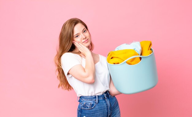 Una bella donna dai capelli rossi che si sente annoiata, frustrata e assonnata dopo una noiosa e con in mano un cesto di lavaggio con i vestiti