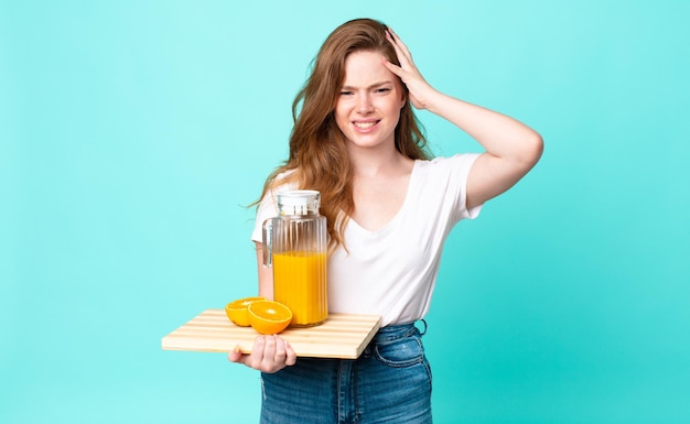 Una bella donna dai capelli rossi che si sente stressata, ansiosa o spaventata, con le mani sulla testa e con in mano un succo d'arancia