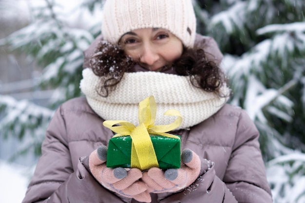 Una bella donna di 45 anni di mezza età che tiene in aria un bel regalo di Natale. Paesaggio innevato con abete rosso e neve