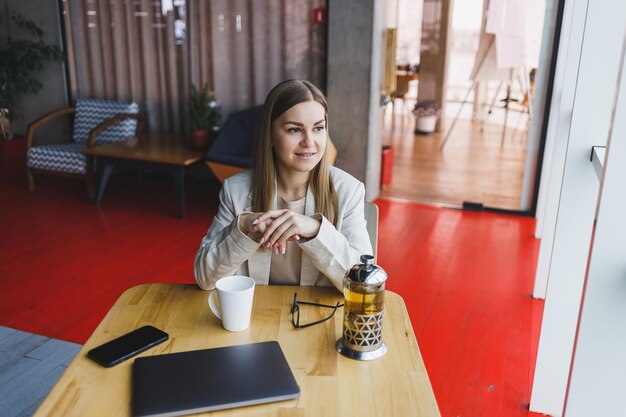 Una bella donna di aspetto sloveno un manager con una giacca leggera e occhiali una ragazza con un sorriso sul viso si siede a un tavolo di legno in un caffè Lavoro a distanza