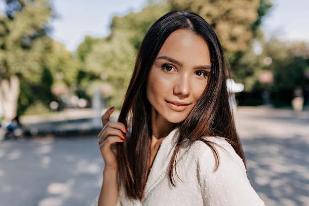 Una bella donna europea con un bel sorriso e capelli scuri è in posa davanti alla fotocamera Una ragazza felice ed elegante sta camminando all'aperto alla luce del sole