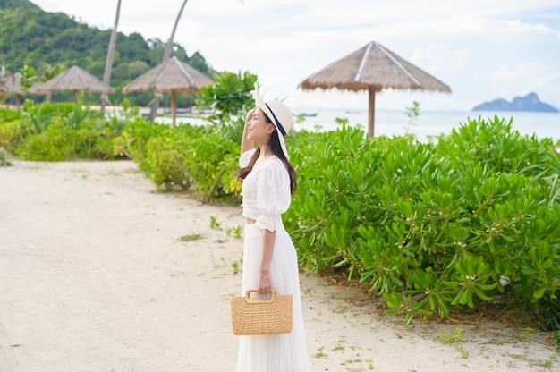 Una bella donna felice in vestito bianco che gode e che si rilassa sulla spiaggia, l'estate e il concetto di vacanze