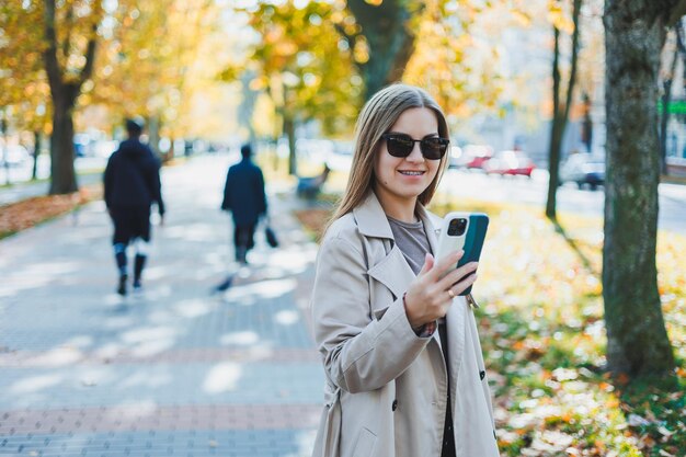 Una bella donna in occhiali da sole cammina nel parco autunnale e parla al telefono Ragazza allegra nel vicolo autunnale della città