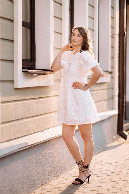 Una bella donna in un abito bianco al tramonto in città Fotografia di strada serale