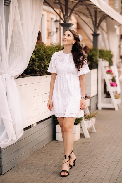 Una bella donna in un abito bianco al tramonto in città Fotografia di strada serale