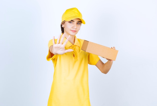 Una bella donna in uniforme gialla con una scatola di carta marrone in bianco che fa il segnale di stop.